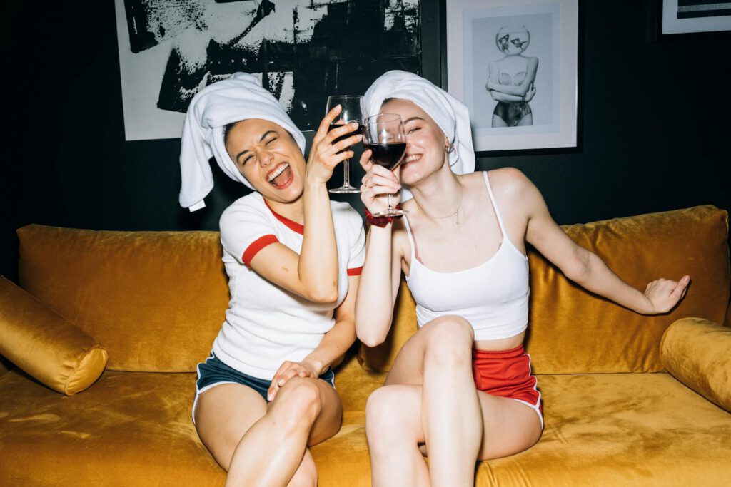 Two women having fun with wine on a yellow sofa, celebrating togetherness.