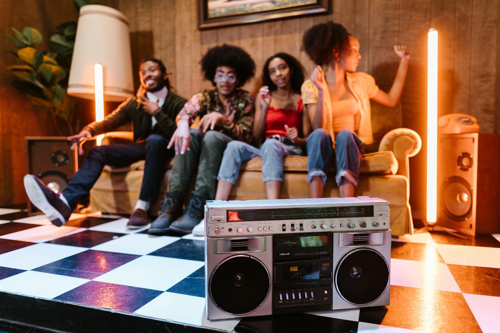 Group of young adults enjoying music in a stylish retro setting with a boombox and neon lights.
